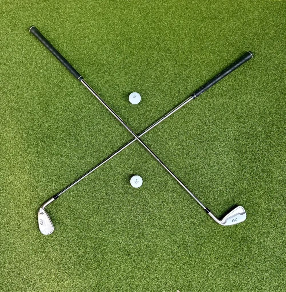 Two golf irons crossed on the simulator turf beside golf balls