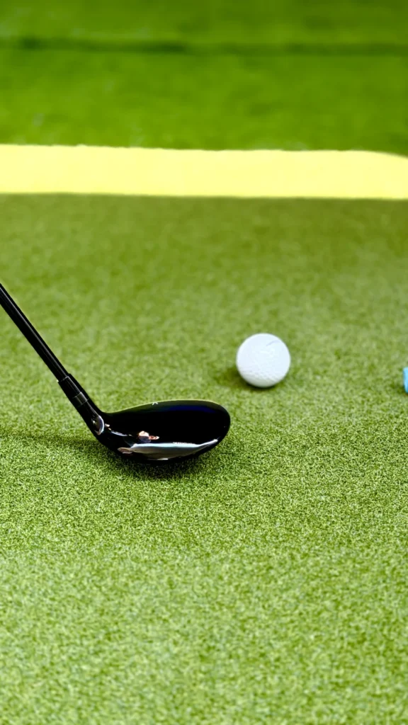 Golf club head at address behind a ball on the simulator hitting mat
