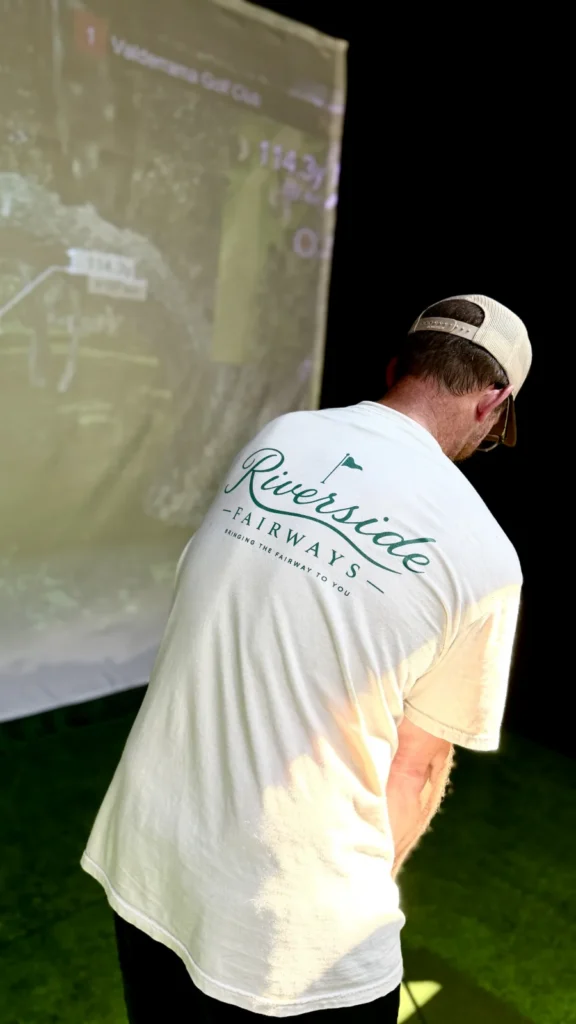 Golfer in a Riverside Fairways branded tee lining up a shot at the simulator screen
