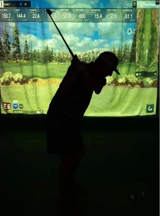 Golfer mid-swing in front of a mobile golf simulator screen showing live shot data