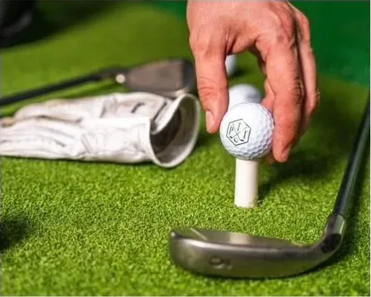 Hand placing a golf ball on the tee before taking a shot on the simulator
