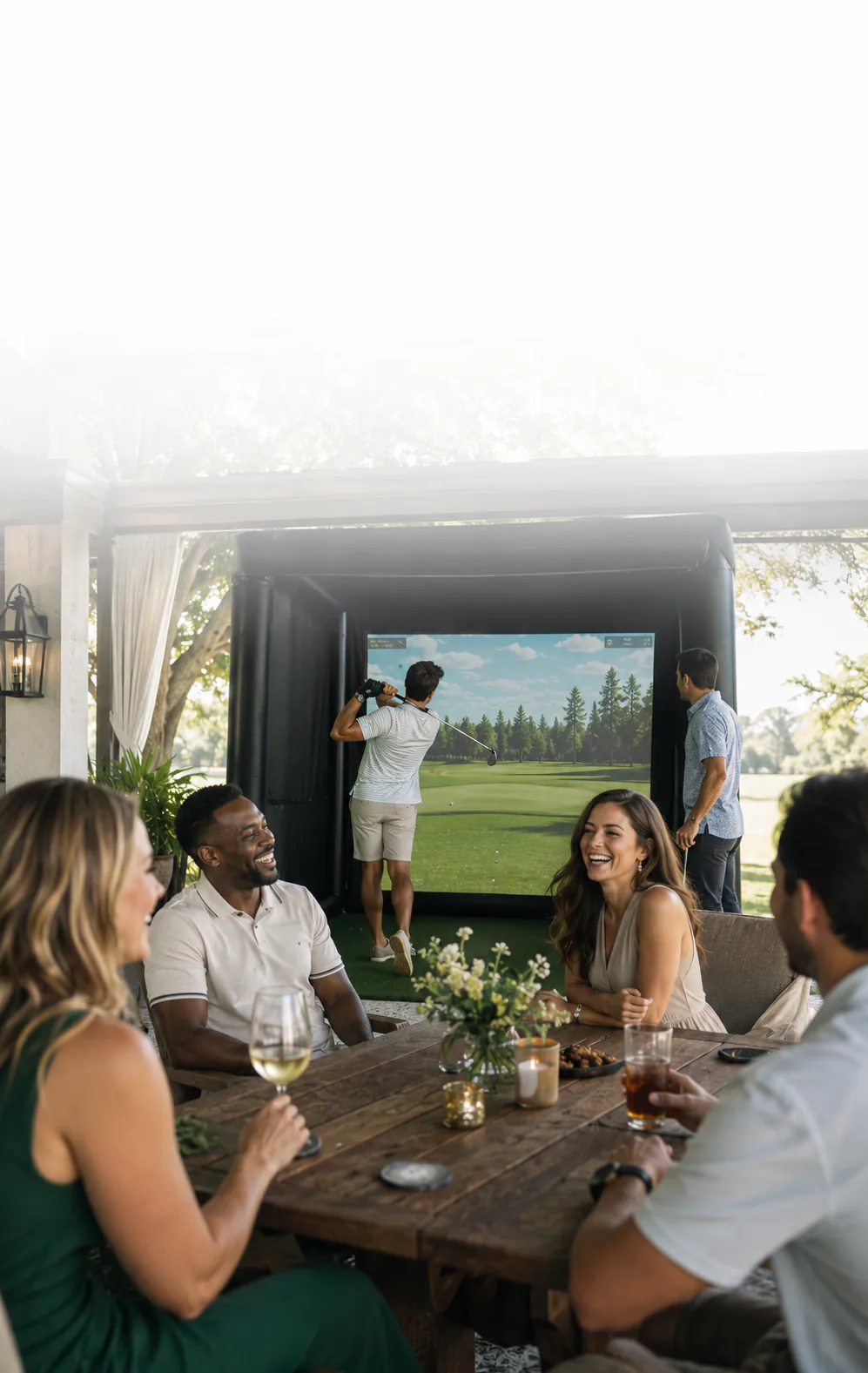 Friends laughing around a dinner table while a guest tees off on the mobile golf simulator