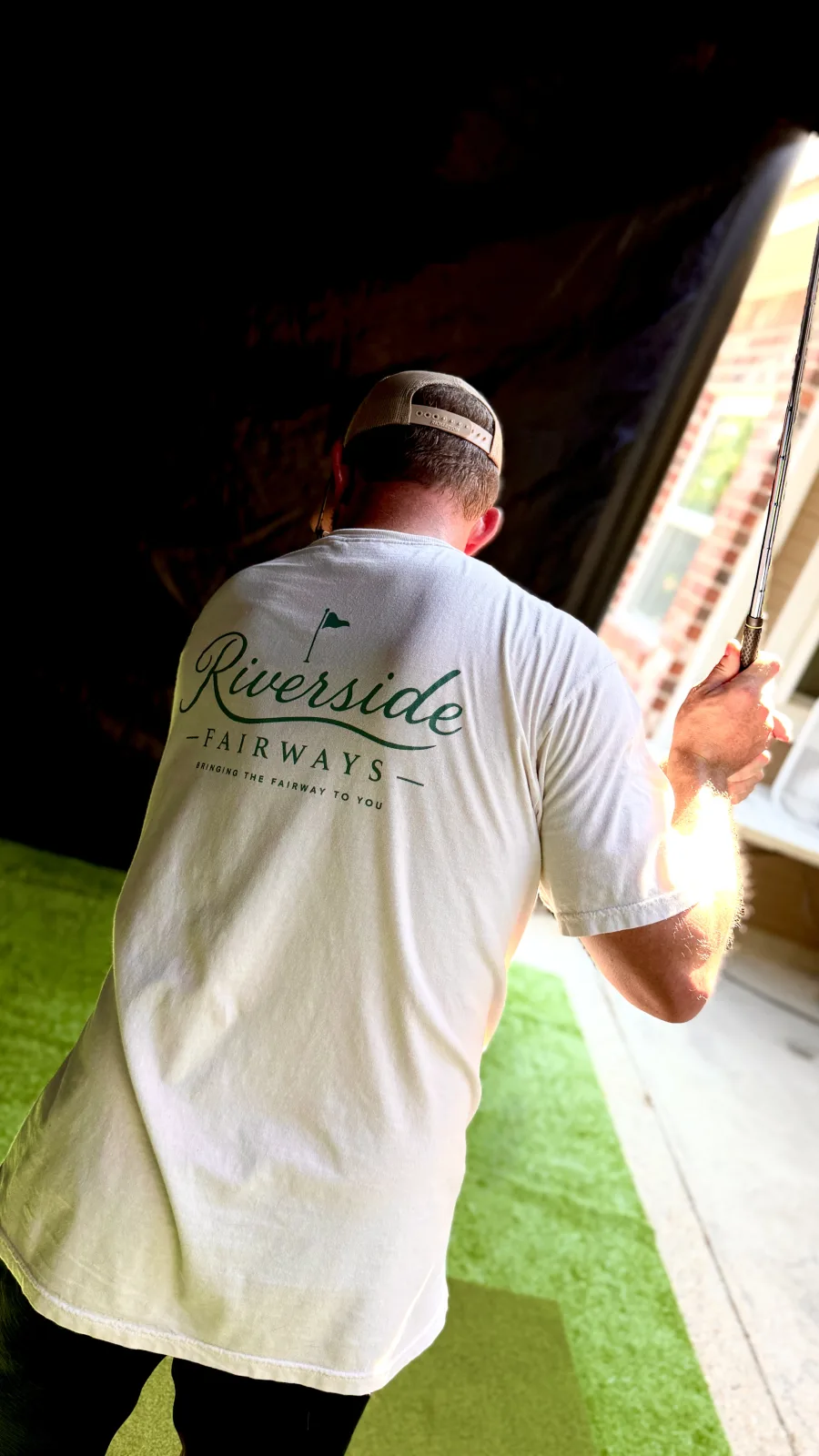 Riverside Fairways owner mid-swing in a branded team tee at the mobile golf simulator