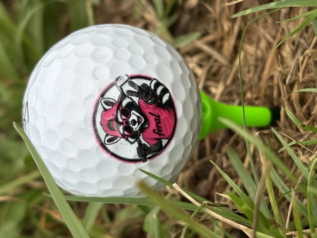 Feral raccoon mascot golf ball on a green tee, close up