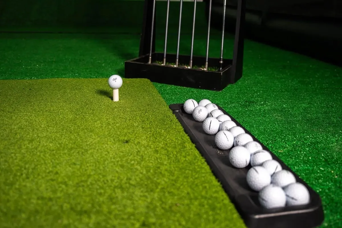 Golf ball on a tee beside the club rack on the hitting turf inside the Riverside Fairways simulator